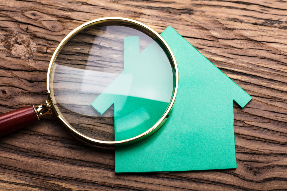 Closeup,of,magnifying,glass,and,green,paper,house,on,wood